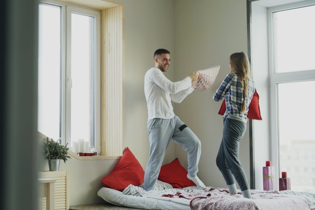 happy and loving couple fight pillows in bed at home in the morning