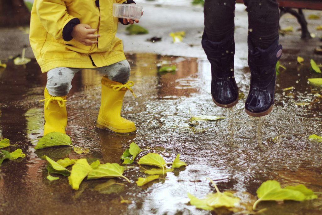 Enfant en ciré jaune et bottes de pluie jouant dans une flaque parmi les feuilles d’automne